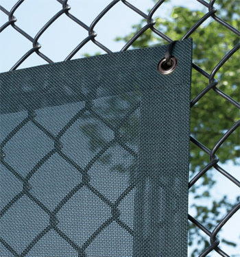 Fencemate windscreen - Dark green privacy screen attached to a chain-link fence with trees in the background