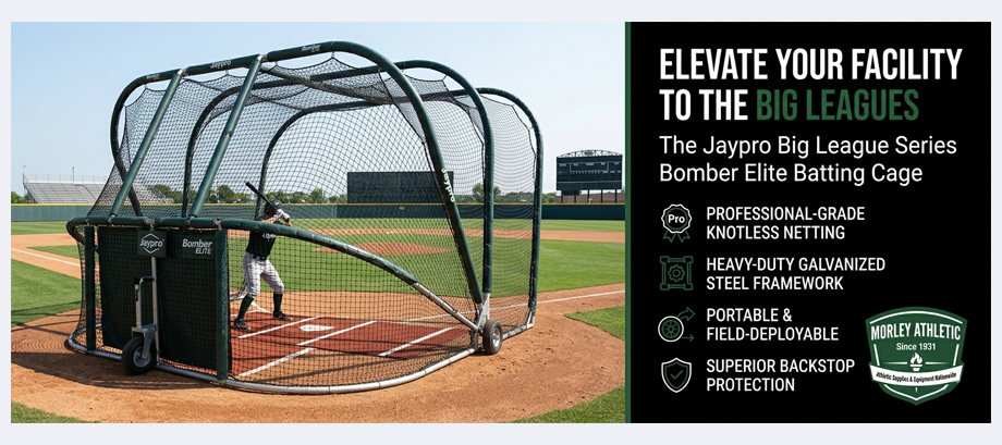 A marketing advertisement featuring a photograph of a baseball player batting inside a dark green, wheeled Jaypro Big League Series Bomber Elite batting cage deployed on a professional-style baseball field with a stadium in the background. Bold text on a black panel to the right states: “ELEVATE YOUR FACILITY TO THE BIG LEAGUES.” Below it, a product description and a list of key features with icons: “Professional-grade knotless netting,” “Heavy-duty galvanized steel framework,” “Portable & field-deployable,