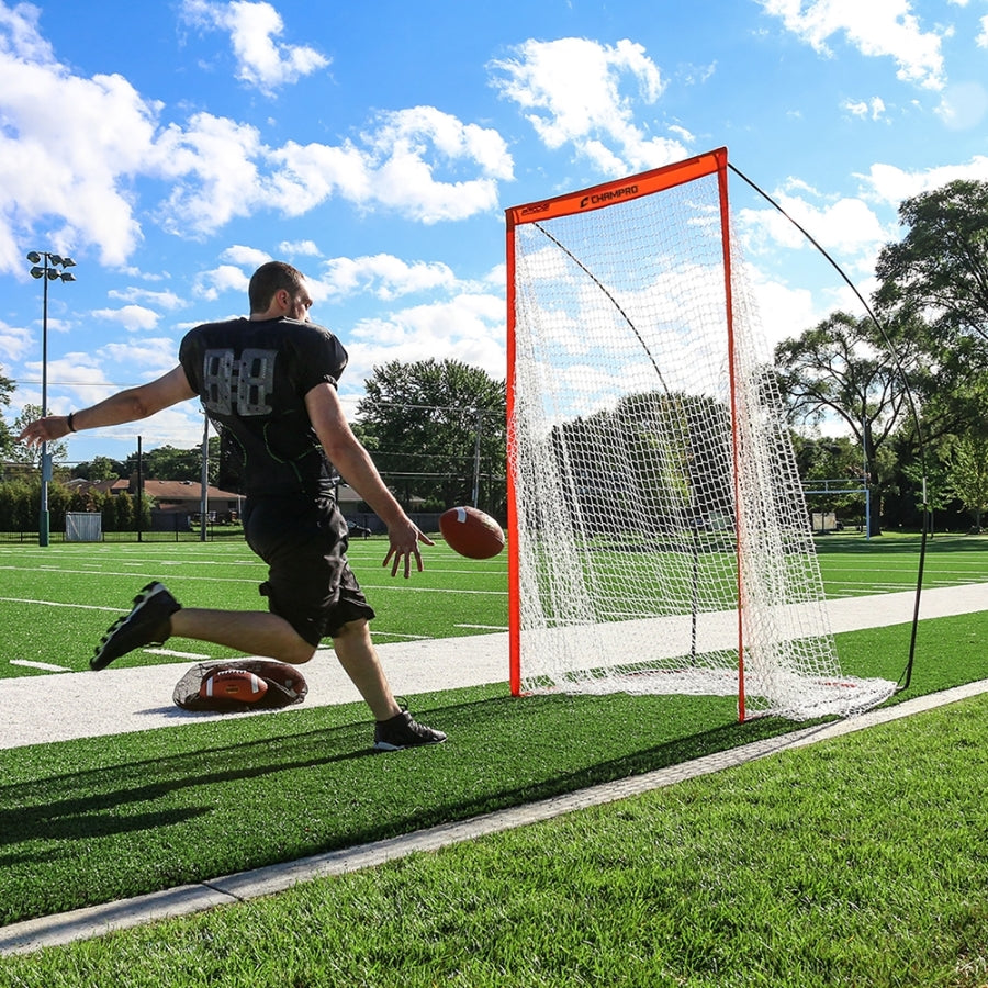 Full front view of the Champro portable football kicking screen set up on a grass field, showcasing its high-visibility orange fiberglass frame and black polyester net.