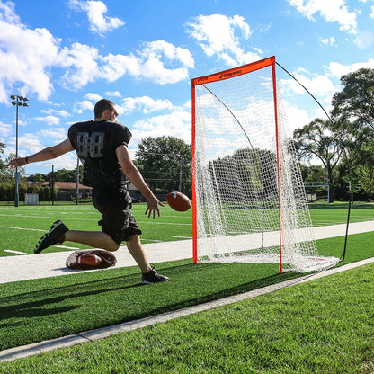 Full front view of the Champro portable football kicking screen set up on a grass field, showcasing its high-visibility orange fiberglass frame and black polyester net.