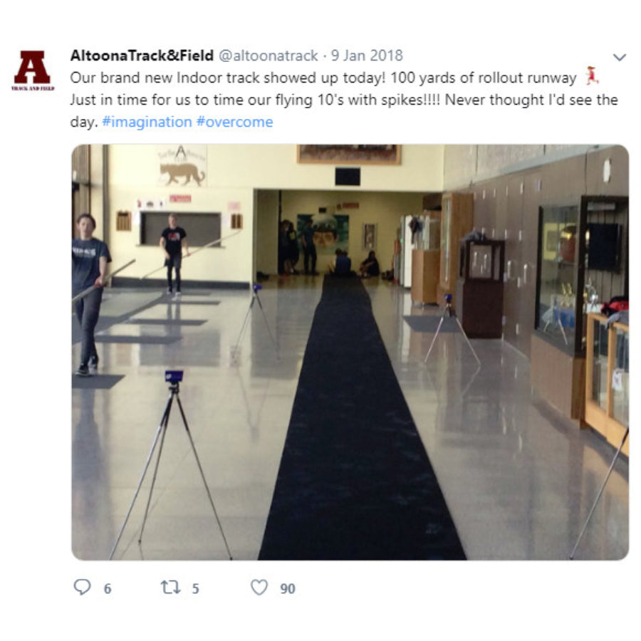 Portable roll-out track runway surface laid out on a practice field, providing a durable and protective rubber lane for triple jump and track events.  Set up in a common hallway area of a high school with timing equipment being used.