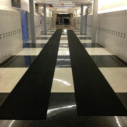 Portable roll-out track runway surface laid out on a practice field, providing a durable and protective rubber lane for triple jump and track events.  2 rolls laid out in the hallway of a high school for indoor off season training.