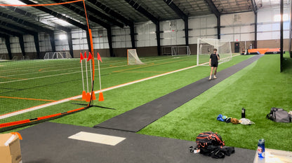Portable roll-out track runway surface laid out on a practice field, providing a durable and protective rubber lane for triple jump and track events. Showing an athlete using the runway indoors.