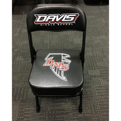 A black deluxe custom sideline chair with a logo on the back, featuring a thick quality cushion and a powder-coated frame, placed on a carpeted floor.