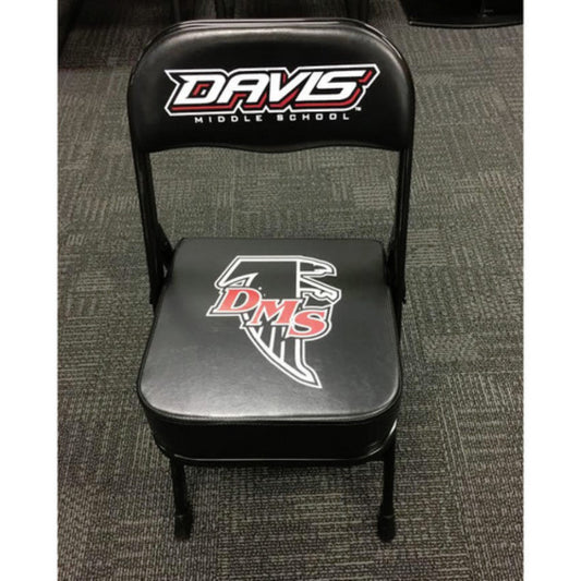 A black deluxe custom sideline chair with a logo on the back, featuring a thick quality cushion and a powder-coated frame, placed on a carpeted floor.